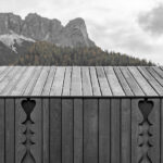 Grau lasierte Lärchenholzfassade mit gefrästen Ornamenten vor Bergpanorama