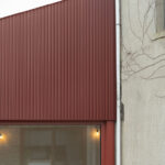 Profilierte Metallfassade in schwedischem Rot neben grauer Putzfassade