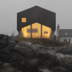 Einfamilienhaus mit schwarzem Dachvolumen und giebelförmiger Glasfassade an der Küste von Tiree