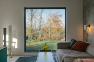 Sitzbereich in einem Ferienhaus mit bodentiefem quadratischem Fenster und Blick in den Garten