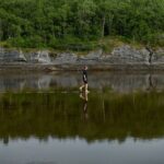 Mensch schreitet über Trittstufen, die von Wasser bedeckt sind - Landschaftsinstallation von Snøhetta im norwegischen Trælvikosen