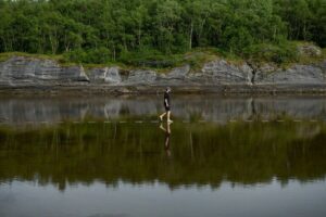 Mensch schreitet über Trittstufen, die von Wasser bedeckt sind - Landschaftsinstallation von Snøhetta im norwegischen Trælvikosen