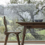 Esstisch mit Stuhl vor bodentiefem Fenster und Natur im Hintergrund