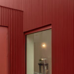 Tür und Fenster in profilierter roter Metallfassade