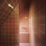 Kleines, rot gefliestes Badezimmer mit Dusche in einem A-förmigen Haus, scharfe Linien und Winkel spiegeln die Form des Hauses wider