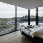Schlafzimmer in einem Strandhaus mit raumhoher Glasfassade und Blick in die Dünenlandschaft