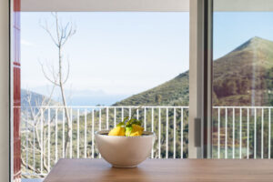 Schale mit Zitronen auf einem Tisch, im Hintergrund begrünte Berge und Meer