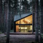 Ferienhaus im Kiefernwald mit schwarzer Holzfassade und schwarzem Aluminiumdach am Abend