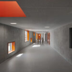 Schulflur in Sichtbeton mit orangefarbenen Akzenten bei Fensterbrüstungen und Oberlicht