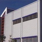 Als Gegengewicht zu den horizontal orientierten Aluminium-Wellprofilen strukturieren die vertikalen Lisenen diese Fassade.