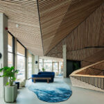 Öffentliches Wohnzimmer mit Kaffeebar und prägnant geformter Holzdecke im Wohngebäude Jonas' von Orange Architects
