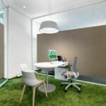 Grüner Boden, weiße Stühle und Tisch unter Lampe vor grauer und weißer Wand mit Schallabsorption:.