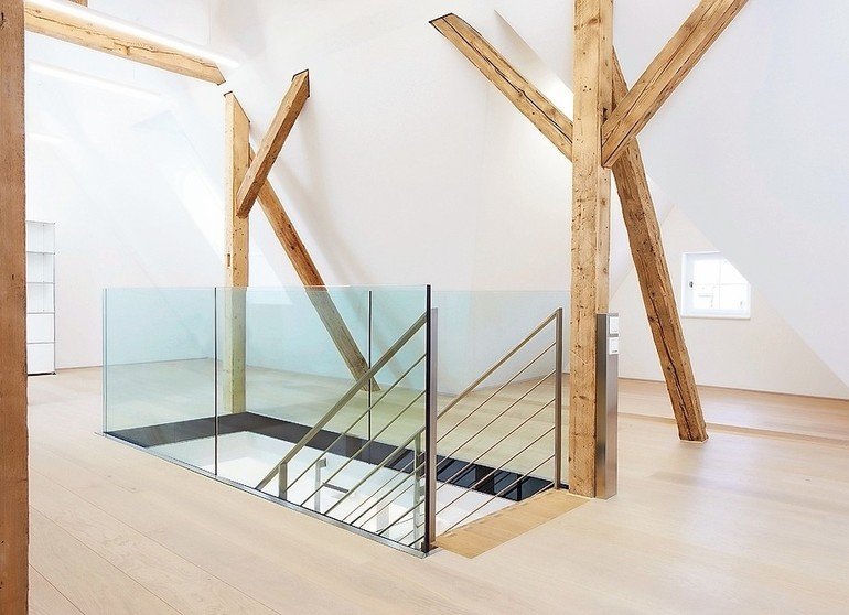 Dachboden eines renovierten Fachwerkhauses mit zentralem, glasverkleideten Treppenaufgang. Bild: Glas Marte