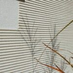 Beige-graue Wand mit vielen Rillen und Schatten von Gräsern: Darunter ein WDV-System.