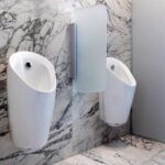 Sanierte Sanitärräume: Weiße Urinale vor marmorierten Flächen.