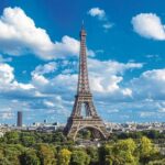 Unter blau-weißem Himmel schmaler hoher Turm vor Stadt, umgeben von Bäumen: Im Eiffelturm-Restaurant werden Abwässer vorschriftsmäßig entsorgt.